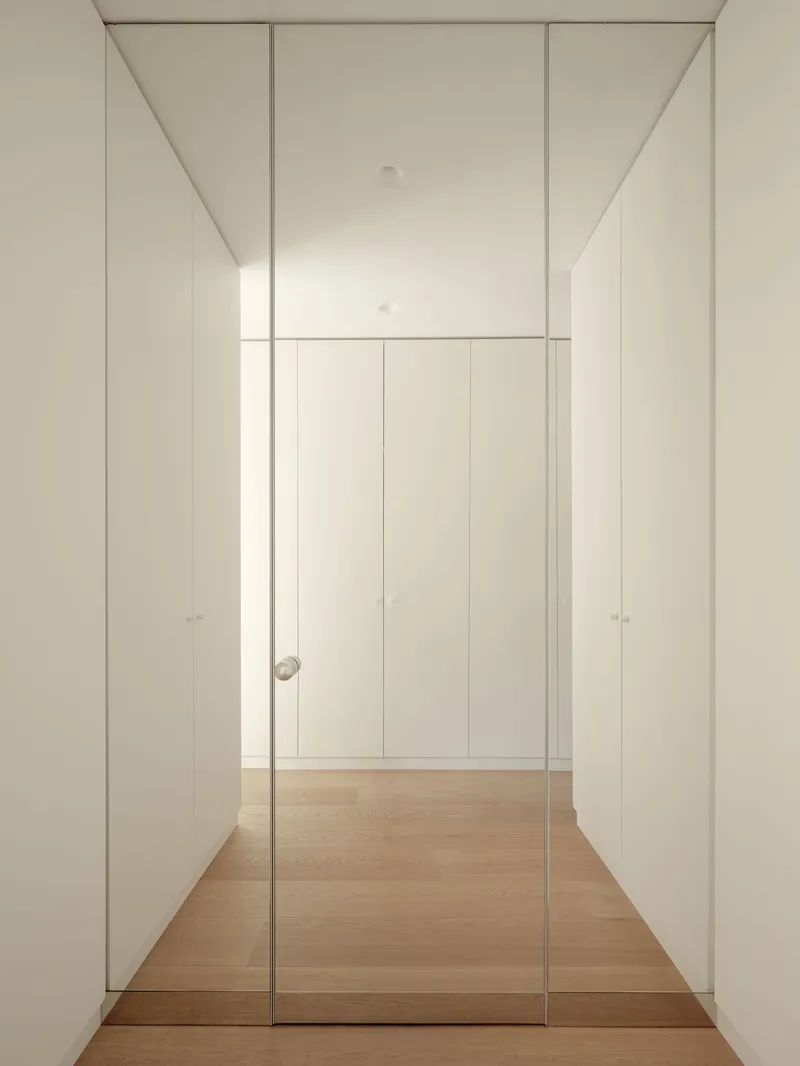 Hallway with floor-to-ceiling white storage panels and full-height glazed door on timber flooring