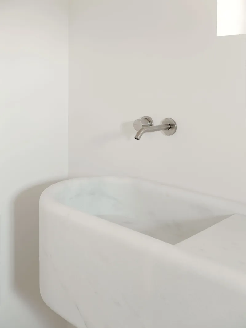 Carved marble basin with rounded edges below a wall-mounted stainless steel faucet