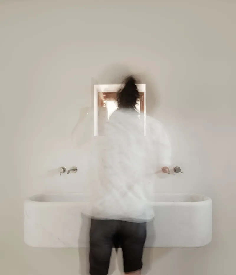 Blurred figure standing at a wall-mounted marble sink with recessed mirror niche above