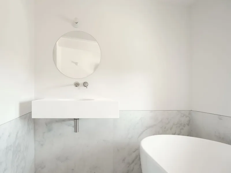 Wall-mounted rectangular basin with circular mirror above marble wainscoting in a corner