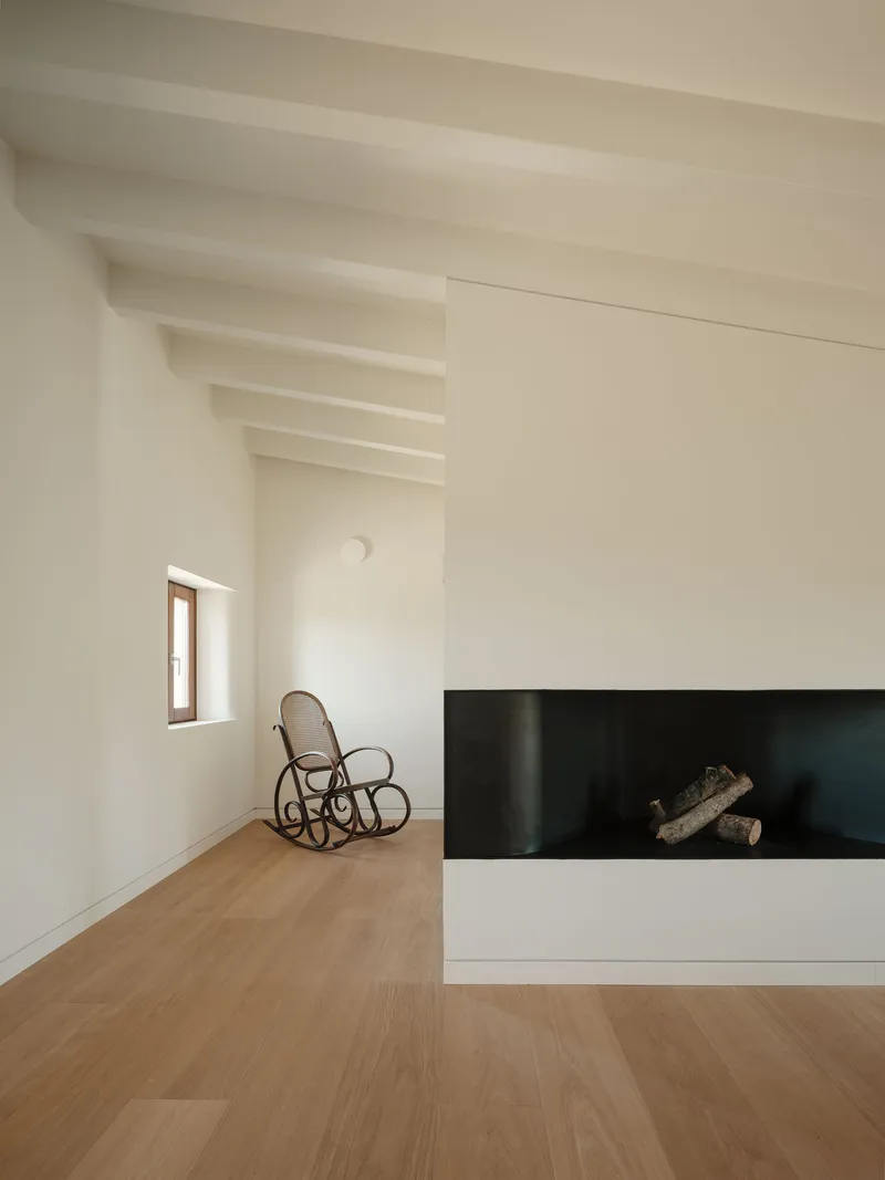 Horizontal fireplace insert with black steel surround beside a bentwood rocking chair under exposed beams