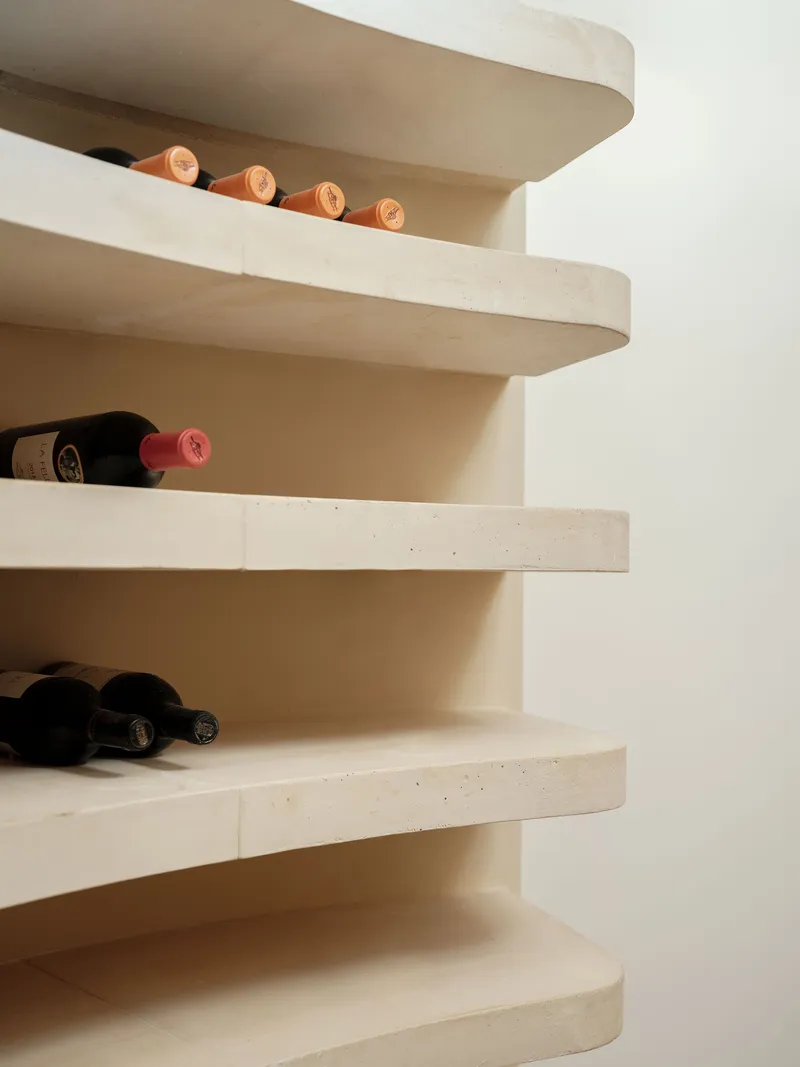 Curved cantilevered stone shelves forming a wine rack with bottles resting on pale treads