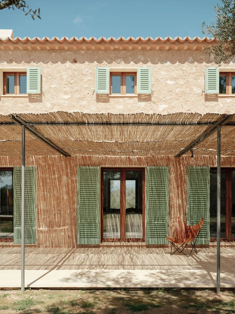 Stone facade with terra cotta tile roof and reed pergola shading glass doors and green shutters