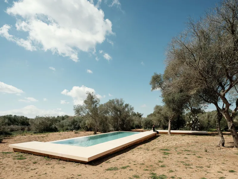 Elevated rectangular swimming pool set in dry landscape under blue sky with scattered clouds