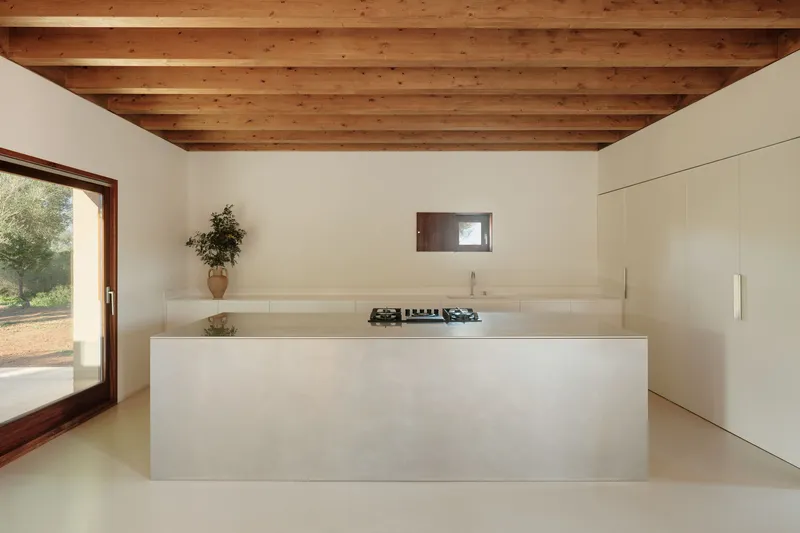 Kitchen island with integrated cooktop beneath timber ceiling and small horizontal window in plastered wall