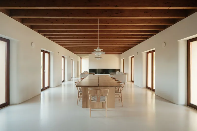 Long dining table with timber chairs centered beneath exposed wooden beam ceiling and pendant light