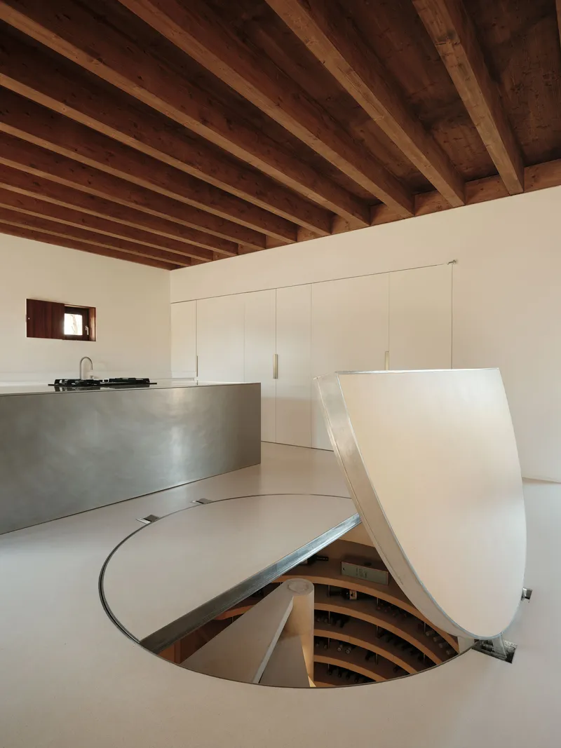 Circular floor opening with curved folding metal cover revealing timber-lined stairwell below