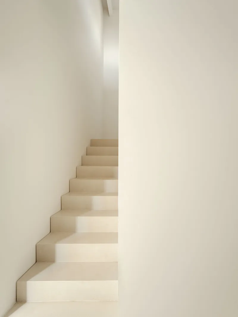 Narrow plastered staircase between converging white walls in soft natural light
