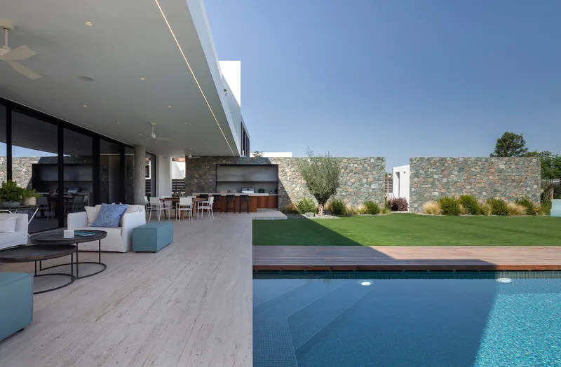 Covered terrace with travertine paving extending from the living area toward the pool and stone boundary wall