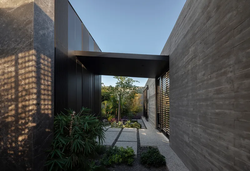 Covered entry passage with perforated stone screen wall and planted courtyard garden under a black beam