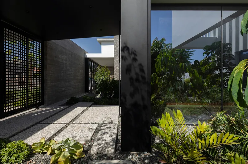 Lattice screen panel filtering dappled sunlight onto a gravel path with tropical planting along the walkway