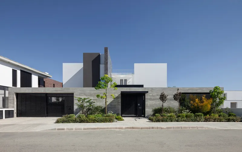 Street view of the facade with perforated metal garage doors and horizontal timber cladding beneath white volumetric forms