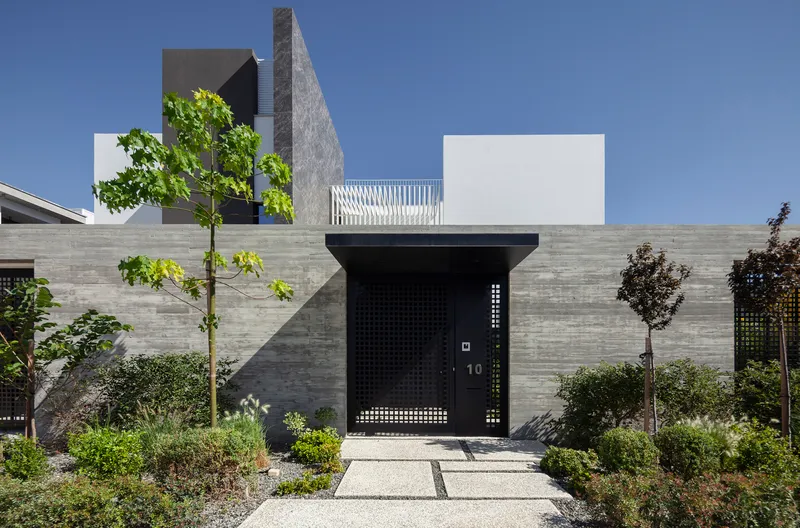 Entry sequence with perforated black metal door set within the horizontal timber wall beside planted garden beds