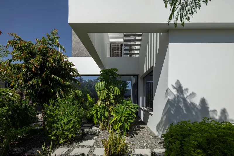 Cantilevered upper volume extending over landscaped courtyard with planted trees and gravel ground surface