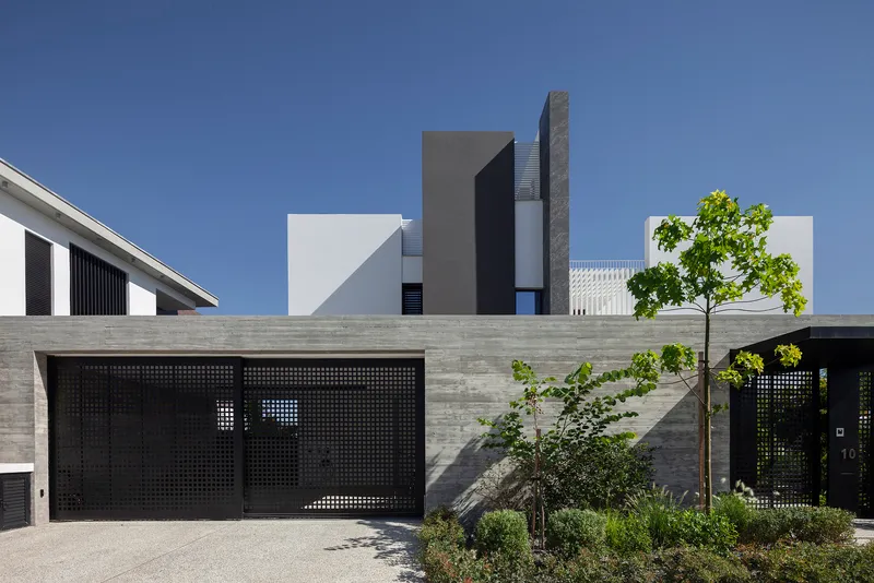 Oblique street view showing the perforated garage screens and stacked white and grey volumes behind planted trees