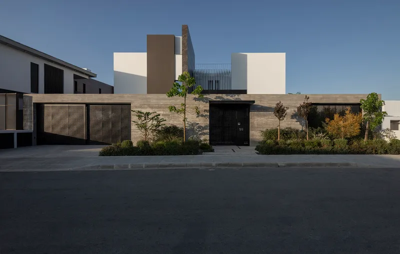 Street view of the perforated metal fence and black entrance door set within a horizontal stone wall