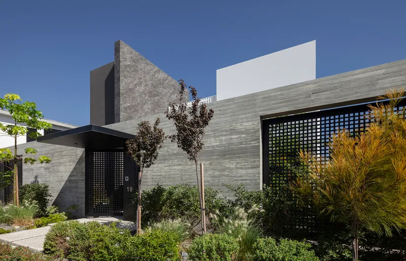 Entrance facade showing horizontal stone cladding and perforated metal screens surrounded by planted shrubs and grasses