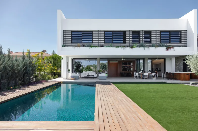 Rear elevation with upper balcony louvers and open ground floor terrace overlooking the swimming pool and lawn