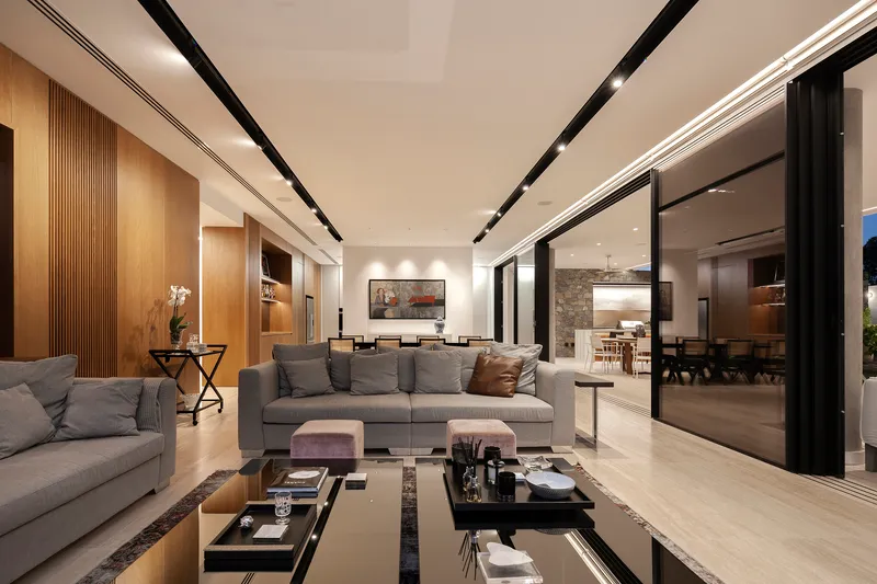 Open-plan living room with floor-to-ceiling glazing opening to outdoor spaces and recessed ceiling lighting tracks