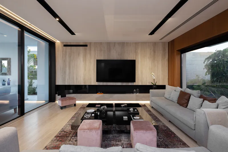 Living space with floating media console beneath wood-clad wall and corner glazing framing garden views at dusk