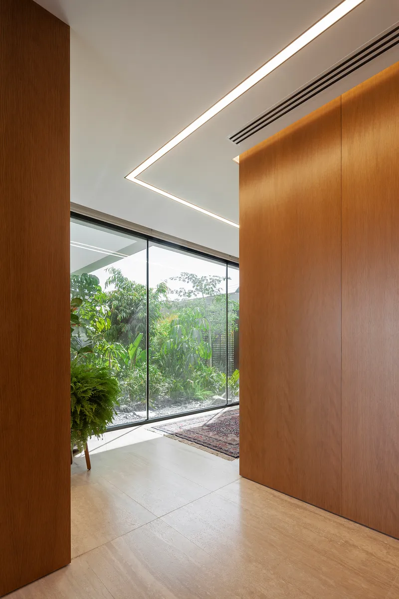 Wood-paneled corridor with angled ceiling light fixture and glazed opening onto garden courtyard