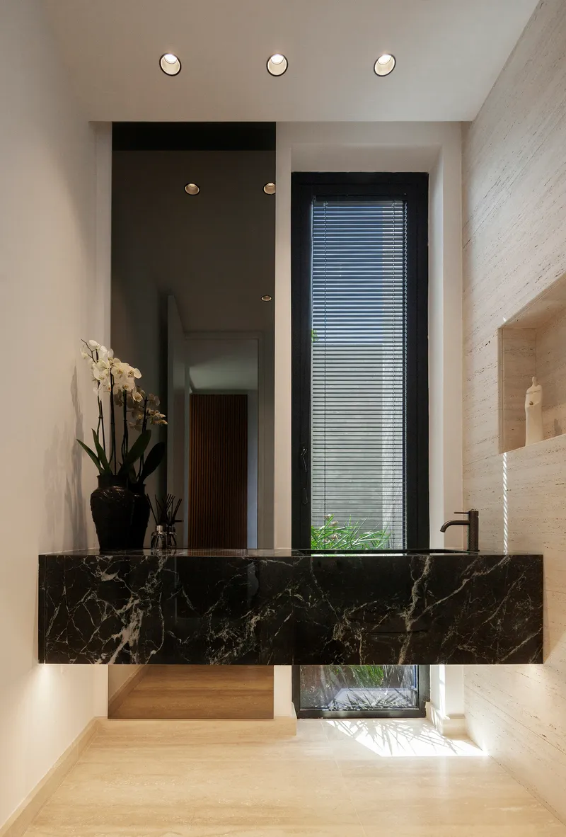 Black marble floating vanity beneath a frameless mirror with narrow vertical window behind
