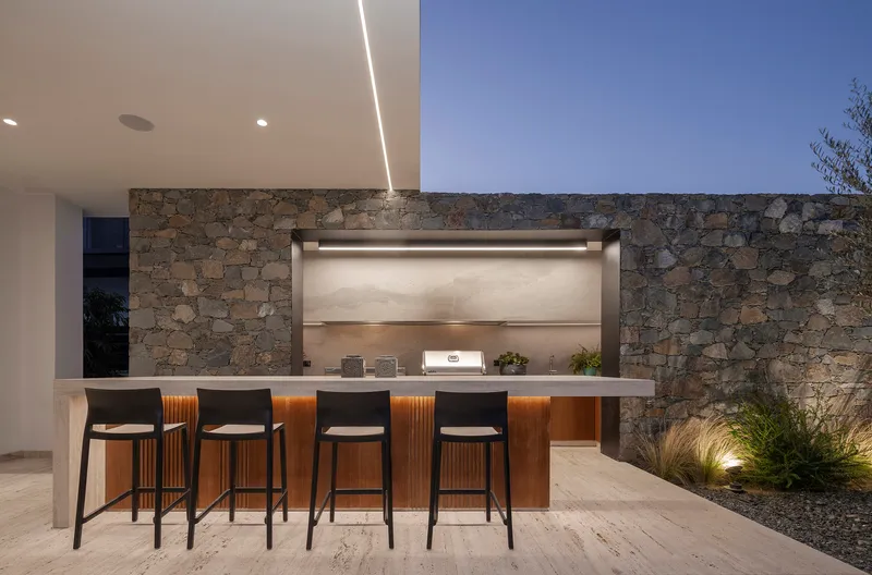 Outdoor bar with stone counter and rubble masonry backdrop under recessed lighting at twilight
