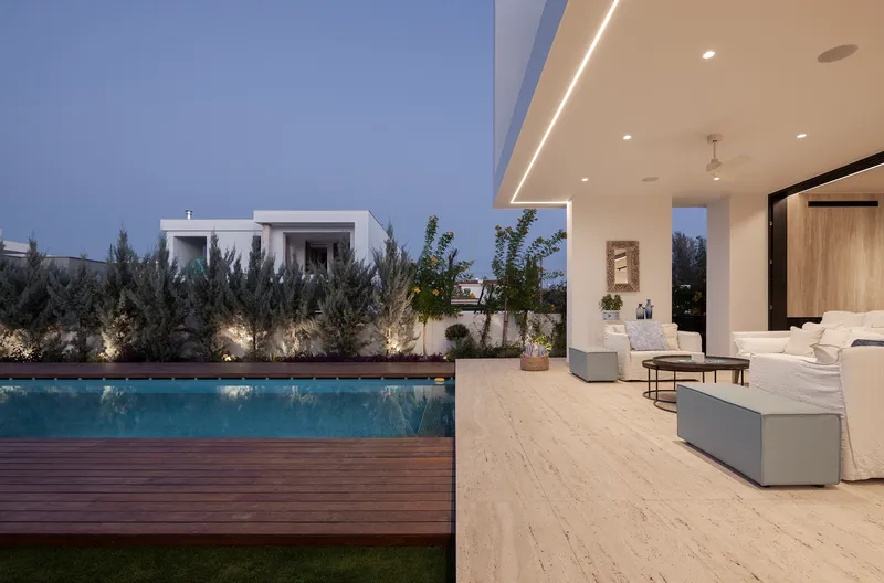 Covered terrace opening to timber deck pool and planted garden at dusk