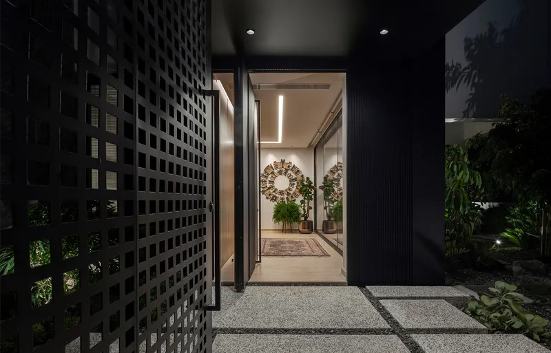Entry path with perforated screen wall and planted garden beds illuminated at night