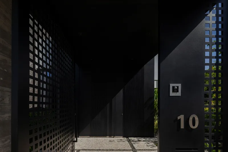 Entry courtyard with perforated black metal screens filtering sunlight onto gravel paving