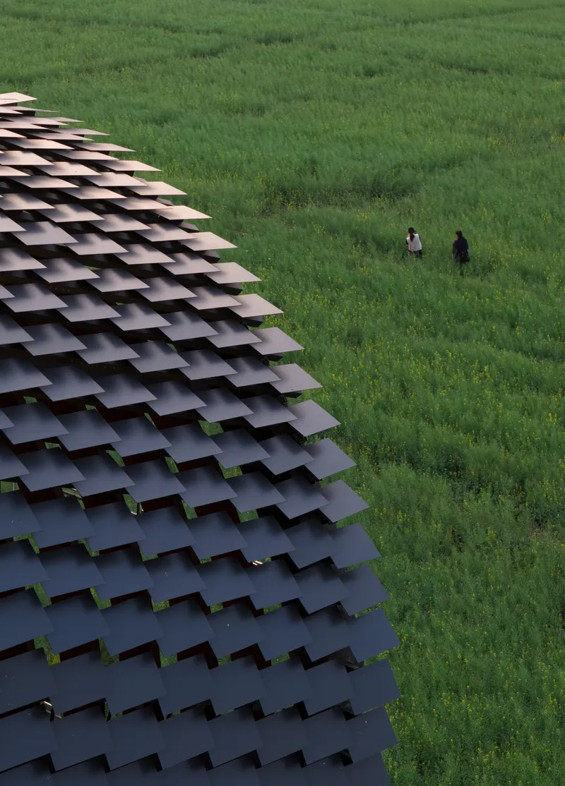 Aerial view of the layered tile canopy edge with two figures standing in the green field