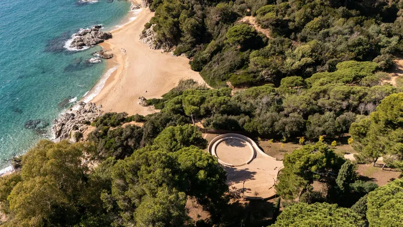 Aerial view of circular pavilion with open oculus nestled in coastal forest above sandy beach