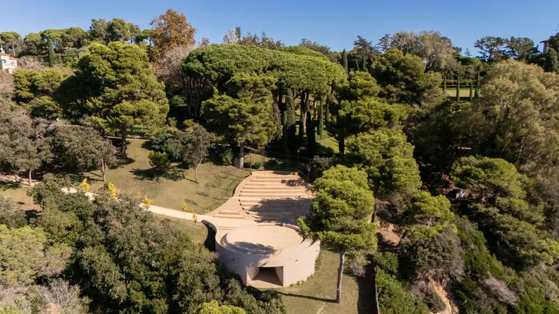 Drone view of curved pavilion with cantilevered roof terrace surrounded by pine trees