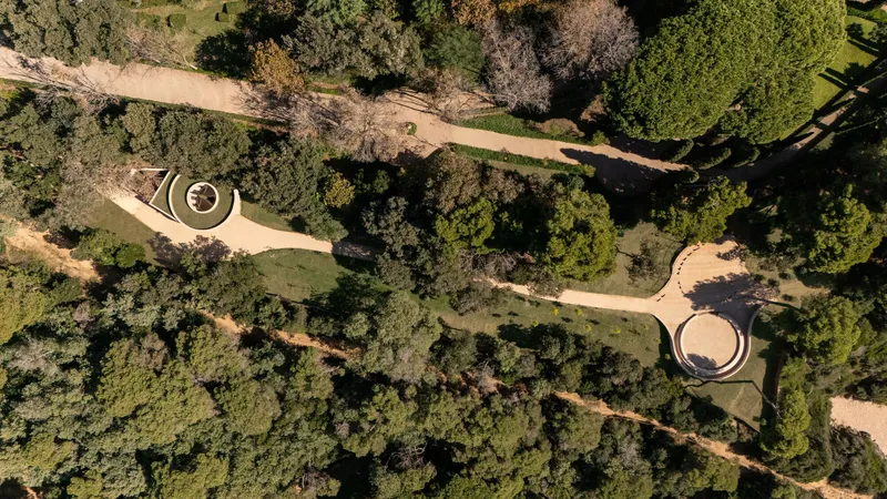 Top-down view of two circular pavilions connected by winding pathways through wooded landscape