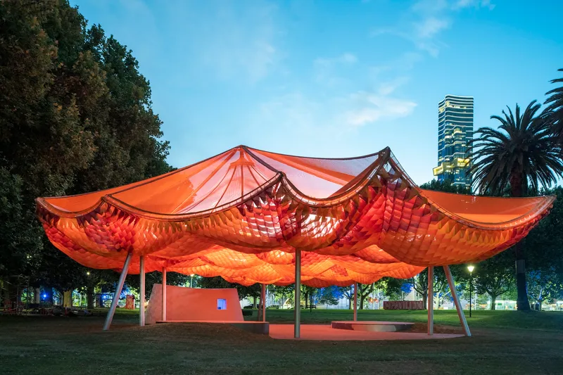 The undulating fabric canopy lit from within at dusk against a darkening sky