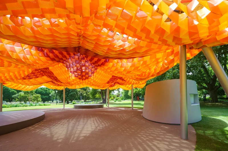 Interior view beneath the orange woven canopy showing light filtering through the geometric openings