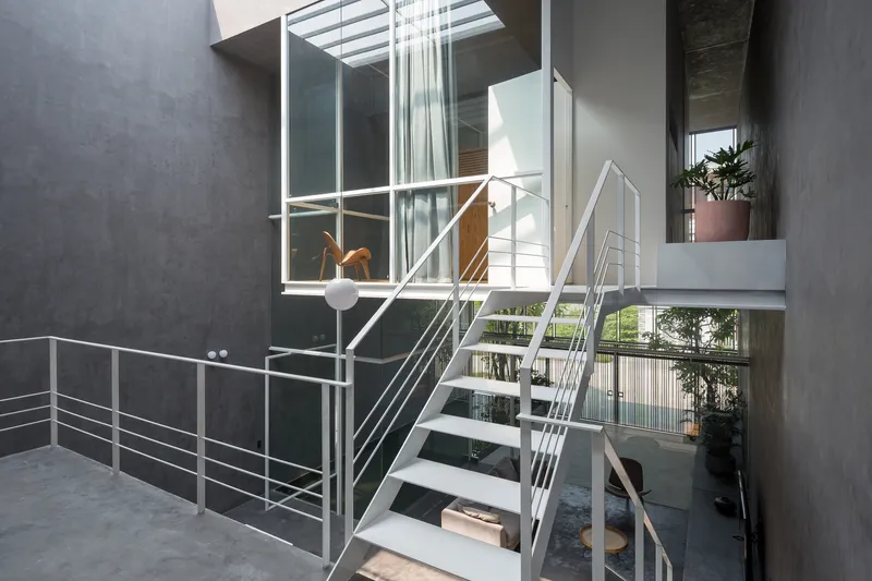 Open-tread steel staircase with cable railings rising through the double-height courtyard space
