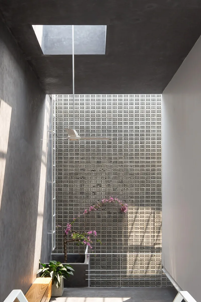 Perforated white brick screen wall with planted balcony beneath a rectangular skylight opening
