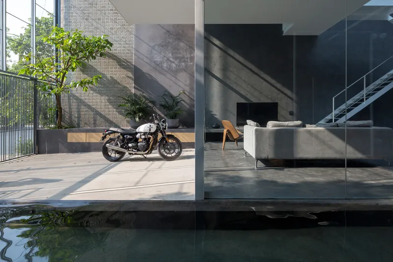 View across a reflecting pool toward the courtyard terrace with motorcycle parked beneath a perforated screen wall