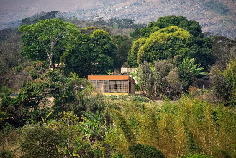 Distant view of the lattice-clad structure nestled among dense foliage with hills in the background