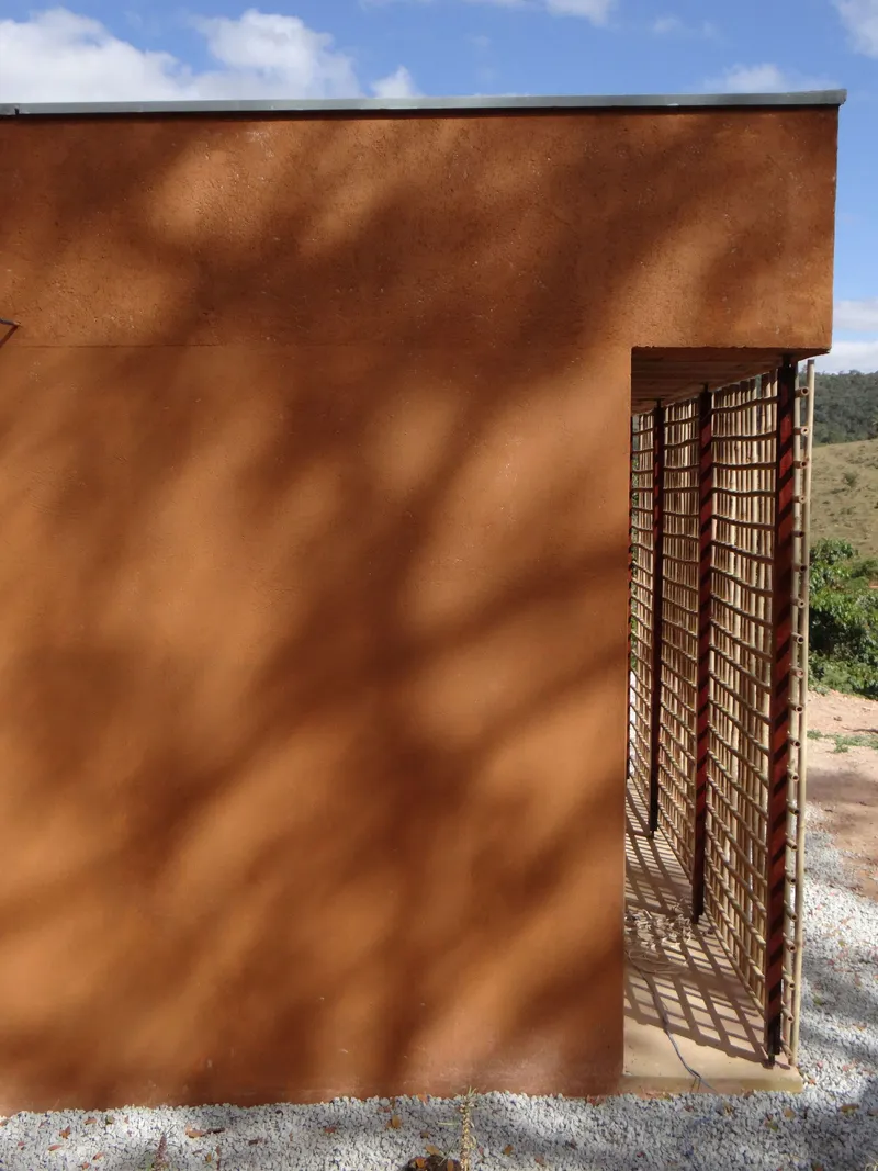 Rammed earth wall with tree shadow patterns beside a recessed lattice screen entry under blue sky