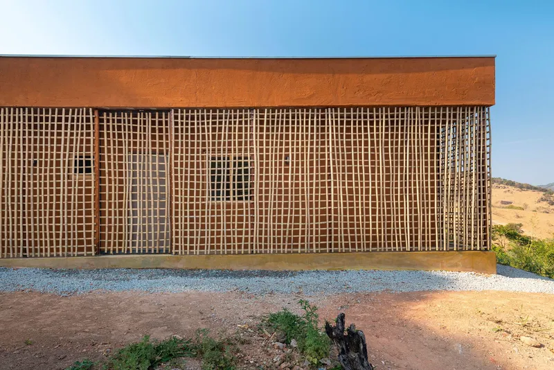Facade with latticed timber screens and rammed earth wall under a blue sky