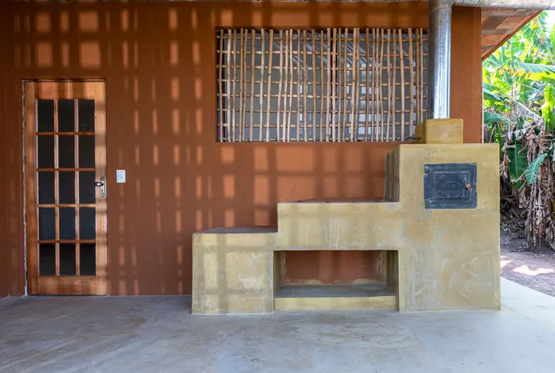 Outdoor living space with rendered earthen fireplace, timber door, and dappled lattice shadows