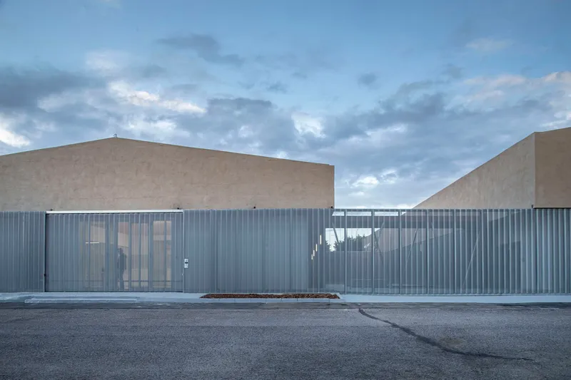 Entrance facade showing glazed openings set within the vertical metal cladding beneath dramatic clouded sky
