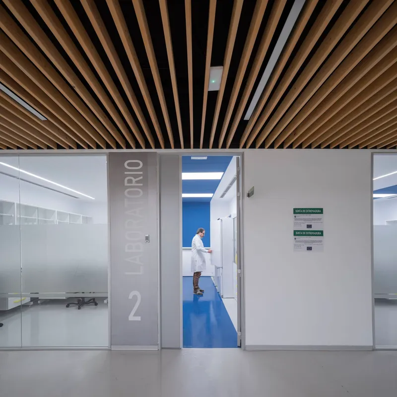 Corridor view through open doorway showing a technician in white coat standing in blue-floored laboratory