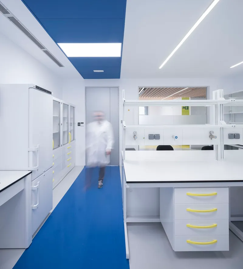 Laboratory interior with white casework and blue resin flooring, one person in motion blur
