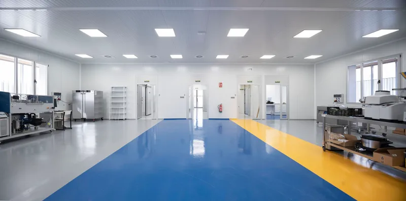 Open laboratory space with blue and yellow floor zones and stainless steel equipment along perimeter