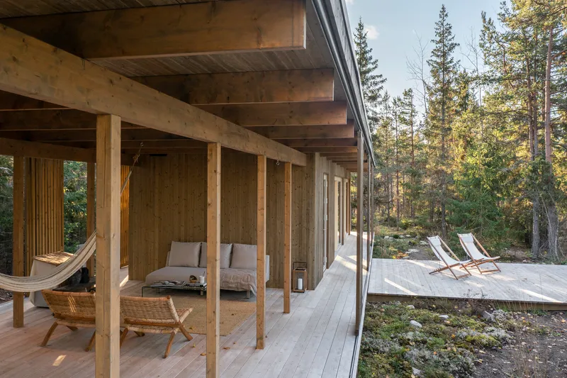 Covered timber porch with exposed columns and beams opening to a forest deck with lounge chairs