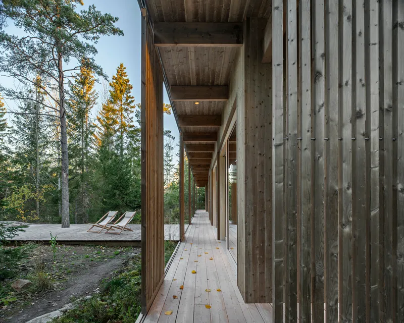 Covered timber walkway with vertical slatted screens and autumn leaves scattered on the decking