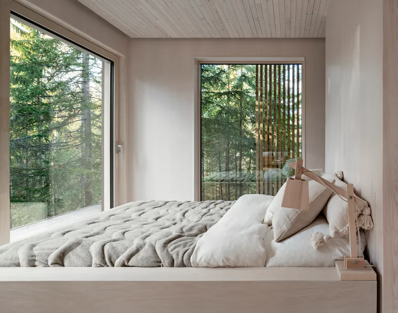 Bedroom with timber platform bed and floor-to-ceiling windows framing views of surrounding pine forest